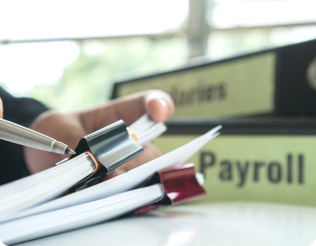 Close-up of a hand holding a pen over binders labeled 'Salaries' and 'Payroll'.